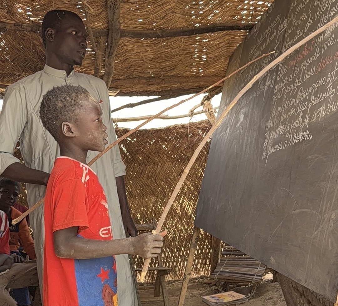 Élève au tableau dans une salle de classe en paille au Tchad